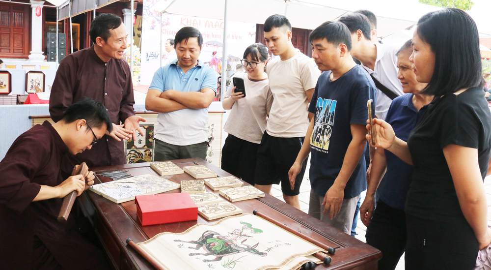 Nghệ nhân Ưu tú Nguyễn Hữu Quả (người đứng ngoài cùng bên trái) cùng con trai là Nghệ nhân Nguyễn Hữu Đạo trình diễn, giới thiệu sản phẩm tranh khắc gỗ Đông Hồ với du khách.